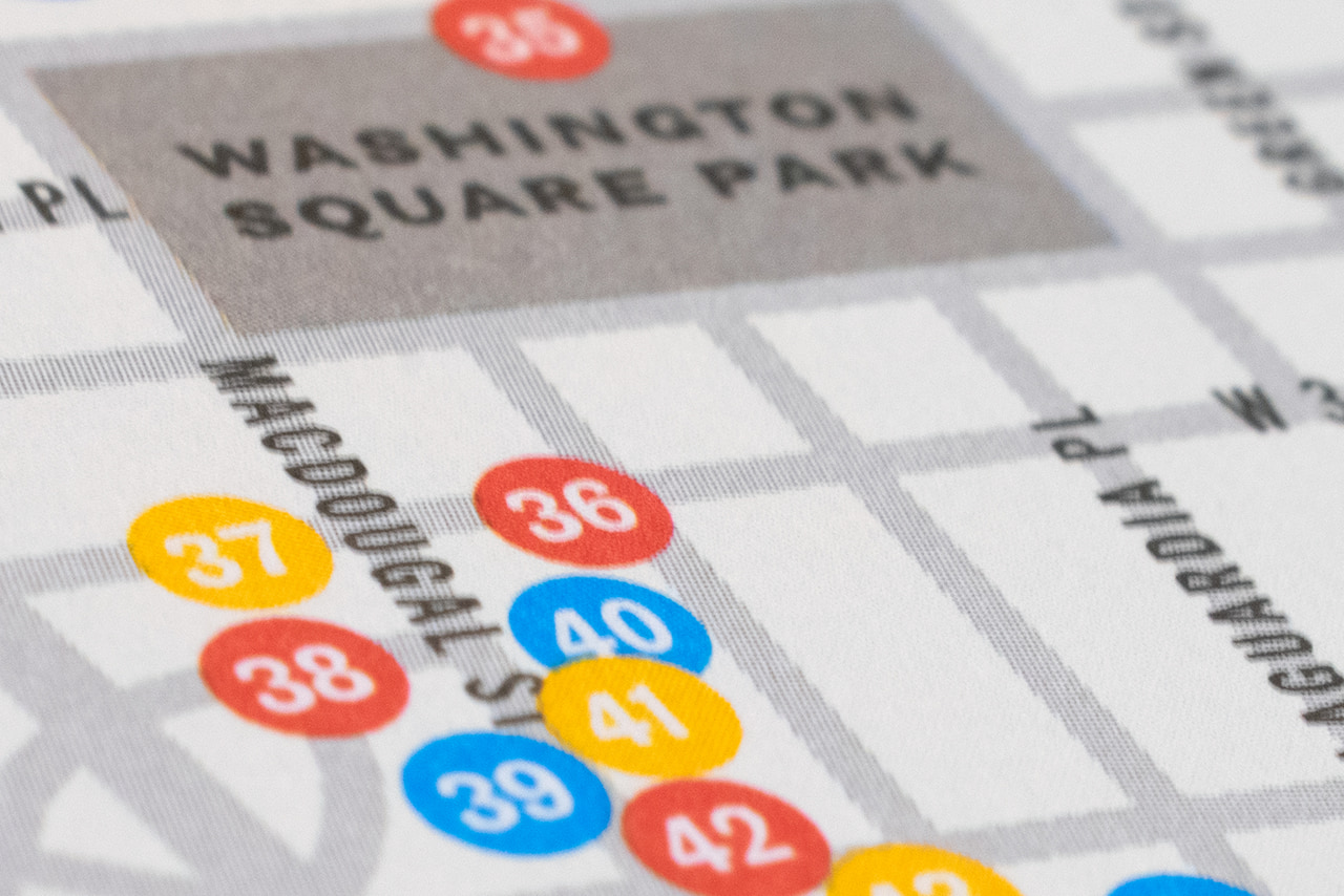 Close-up of the printed Greenwich Village map around Washington Square Park, showing street names and numbered colored location markers.