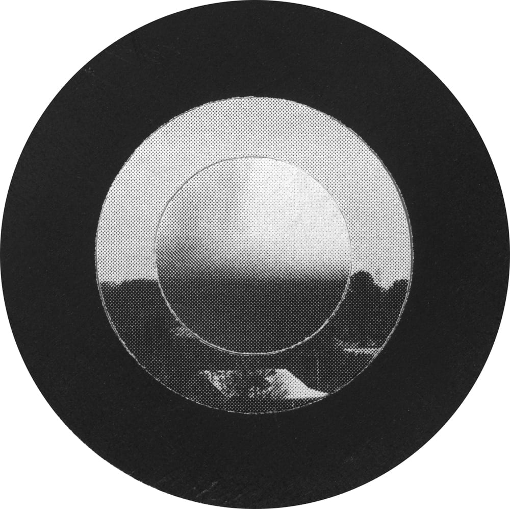 Black circular field surrounding a pale halftone ring and a central landscape photograph.