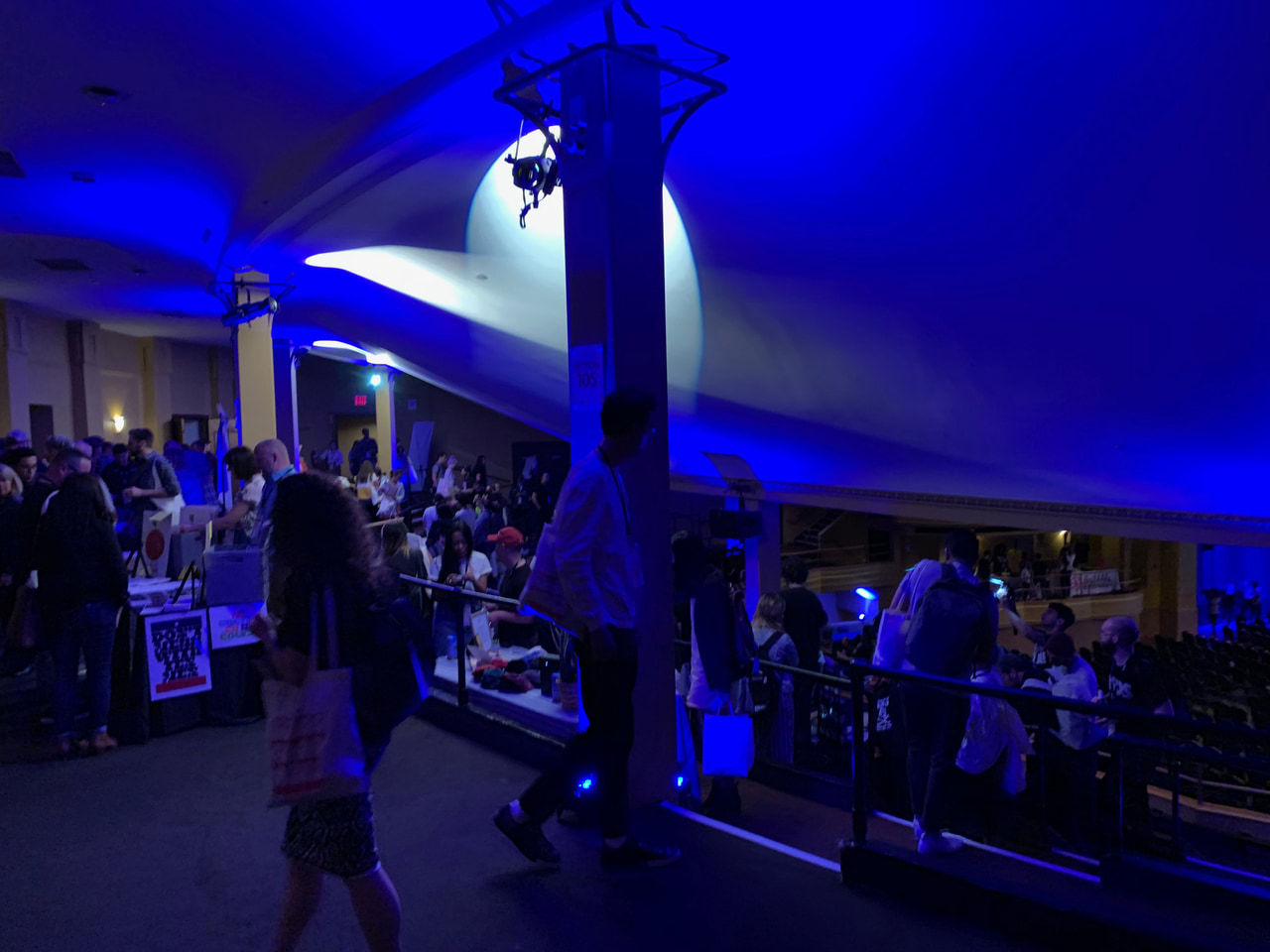 People mingling in a theater lobby lit in deep blue.