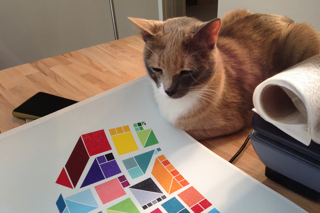 Orange-and-white cat beside a colorful map print and a roll of white paper on a wooden table.