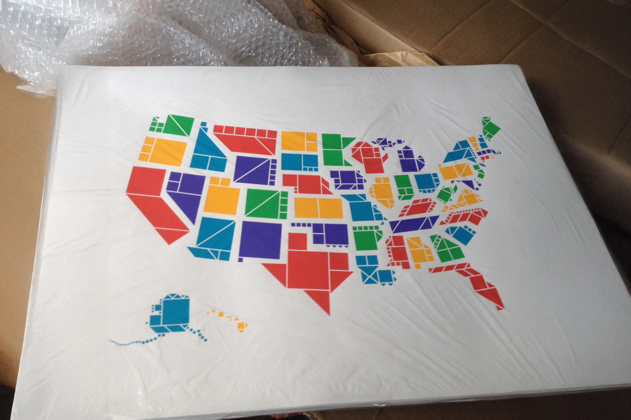 Tangram States United States map print wrapped in clear protective plastic on a wooden floor.