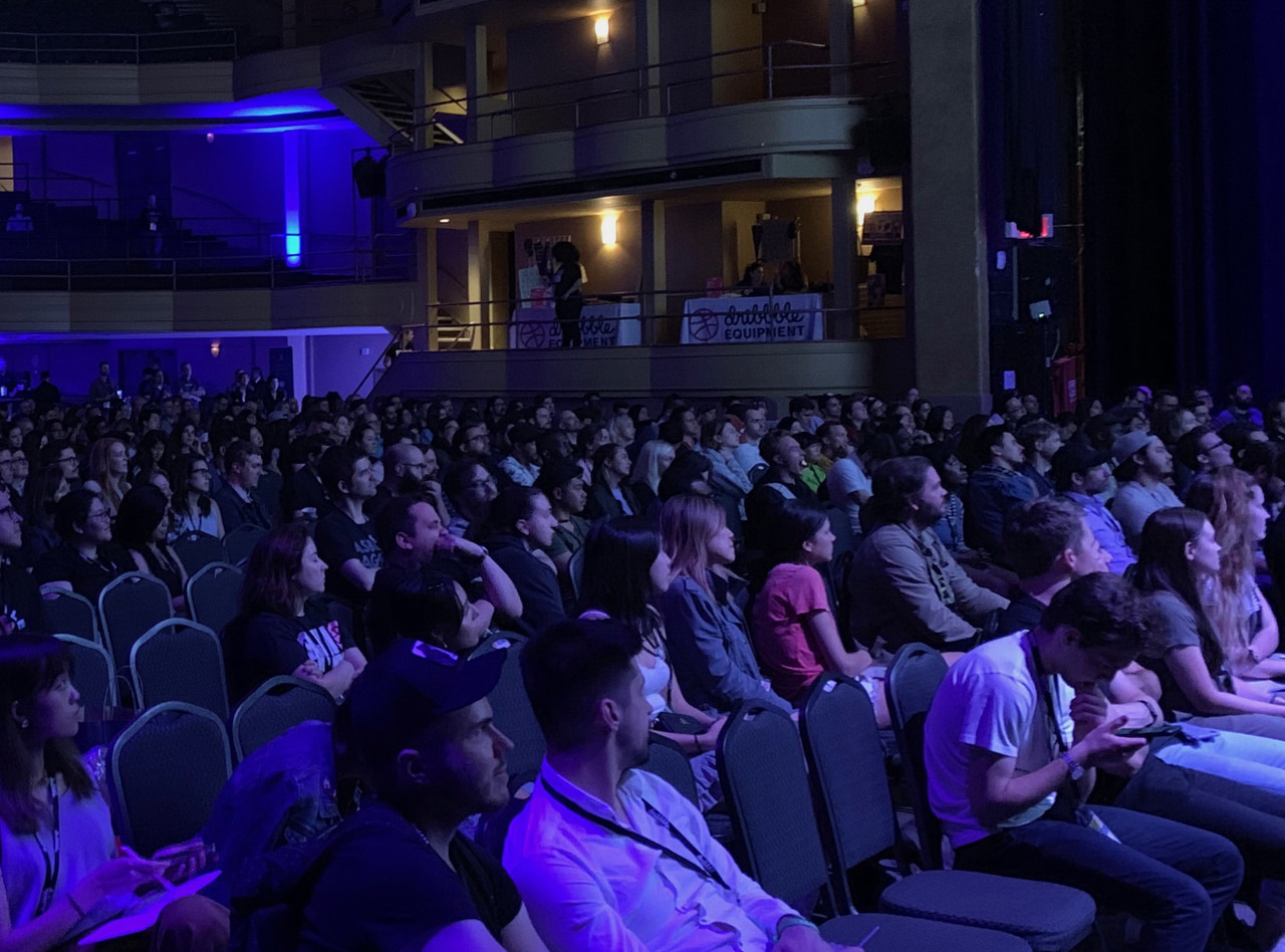 An auditorium audience under blue stage lighting.