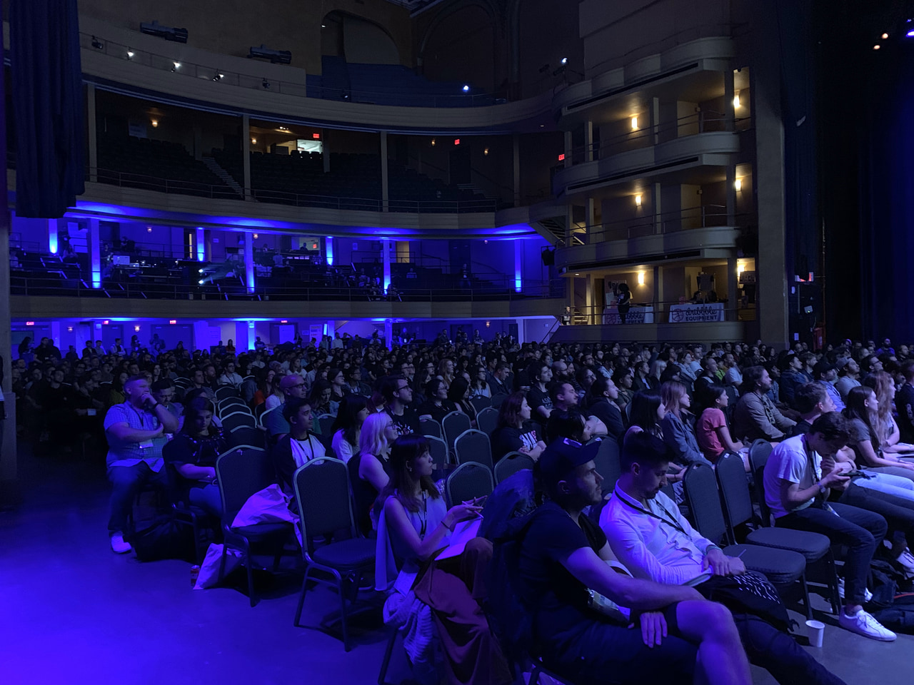 An audience seated in a theater under blue lighting.