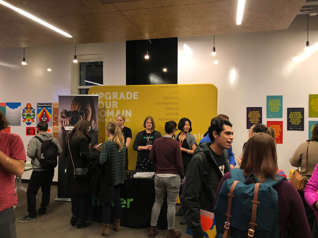 People talking in a crowded indoor design gathering, with colorful artwork displayed on the walls.