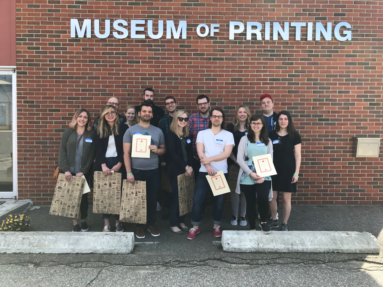 Group photograph outside a brick building beneath the Museum of Printing sign, with several participants holding prints.