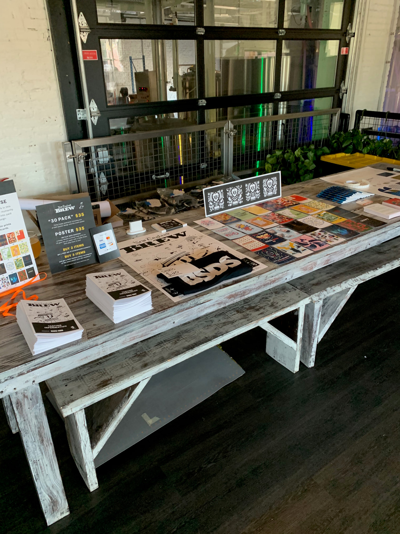 Table of prints and publications beside large windows, with two ornamental black-and-white prints propped at the back.