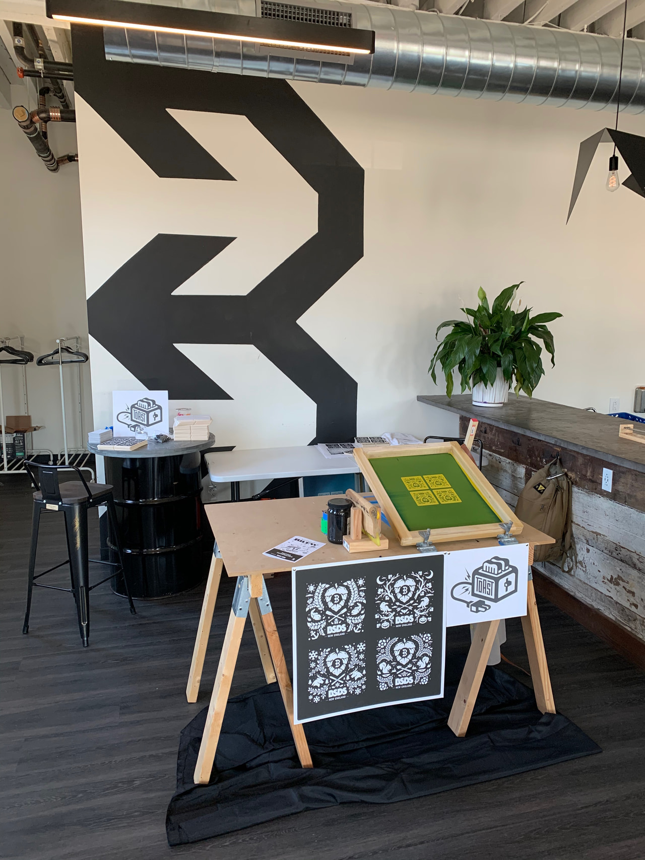 Screen-printing equipment and displayed black-and-white prints in a room with large black arrow shapes on a white wall.