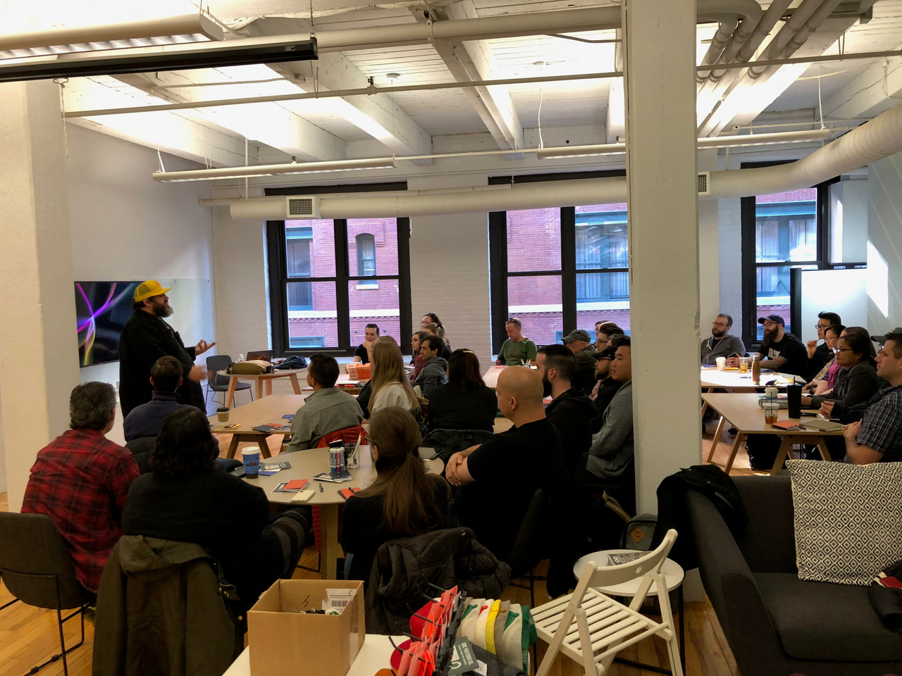 Workshop participants seated in rows facing a presenter in a bright room with large windows.
