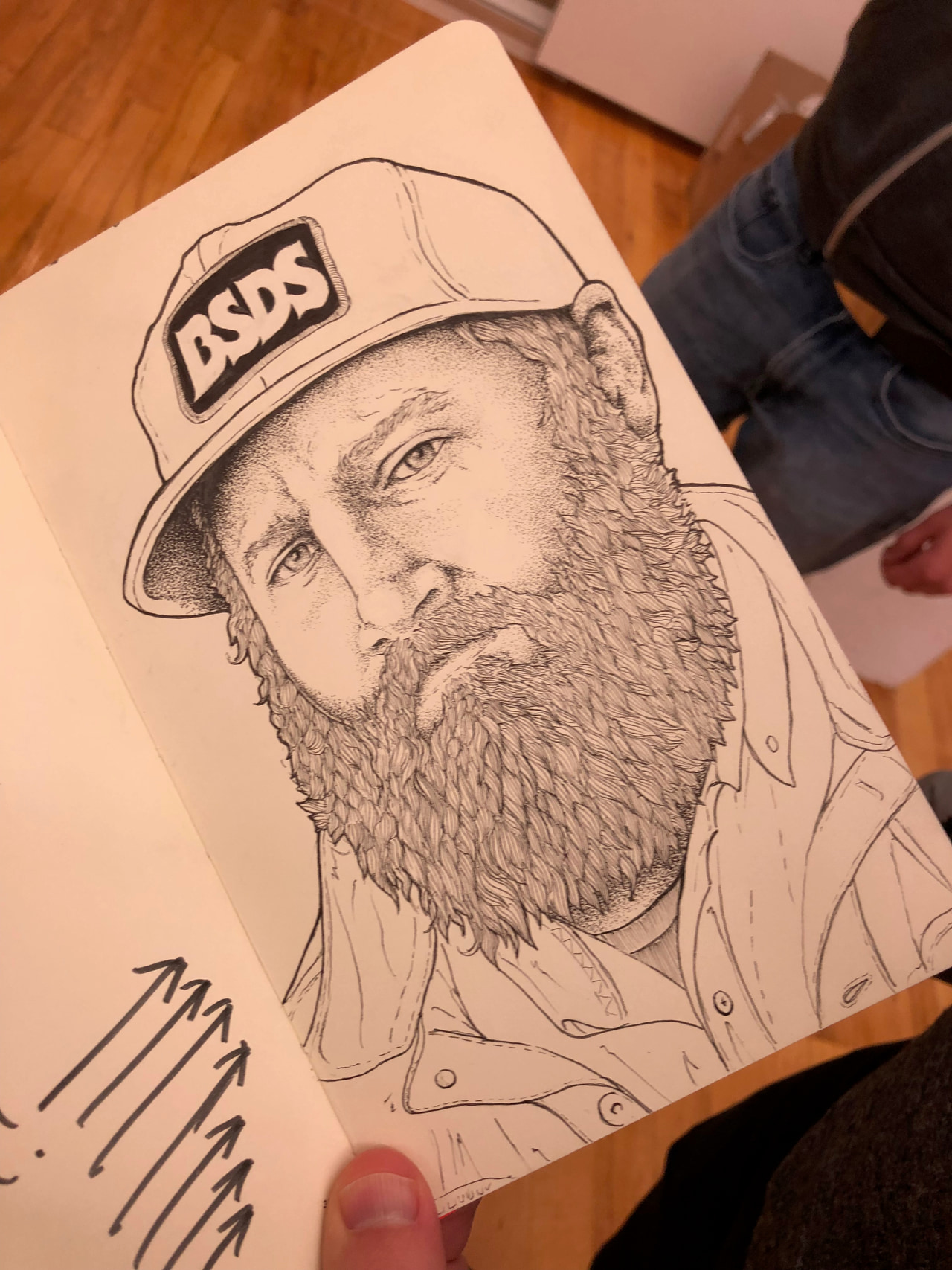 Signed line drawing of a bearded person wearing a BSDS cap, held over a wooden floor.