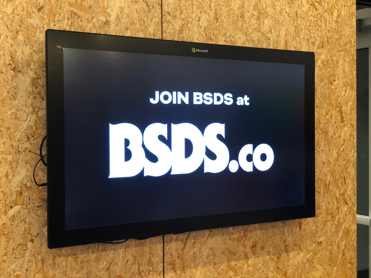 Wall-mounted screen reading Join BSDS at BSDS.co in white lettering on black.