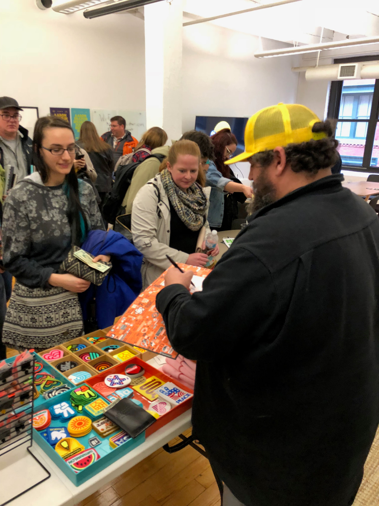 Person in a yellow cap presenting colorful printed work to a small group at a workshop table.