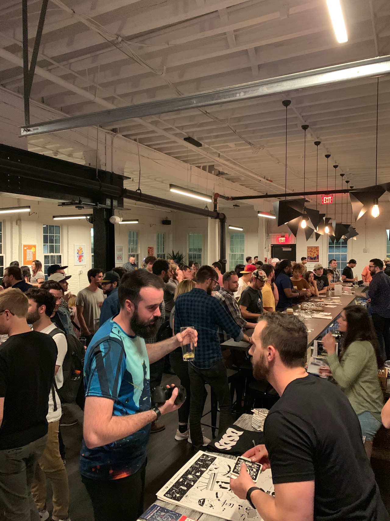 Crowd talking around a table of printed artwork inside a gallery.