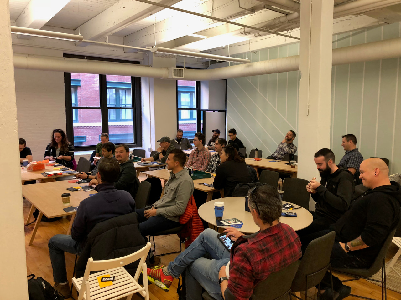 Workshop participants around tables with papers and supplies in a room with large windows.
