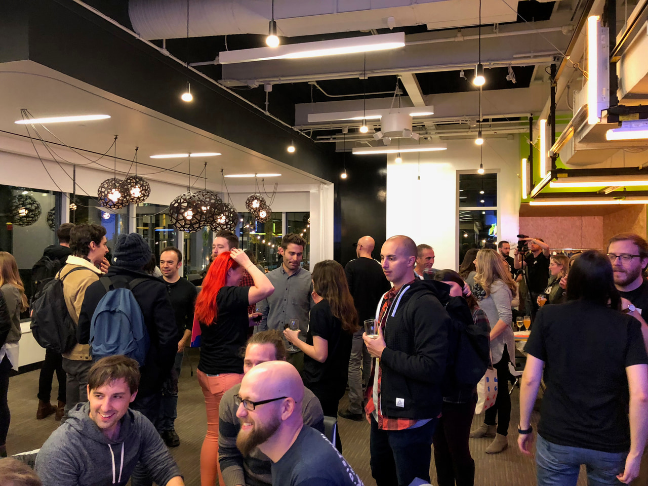 People gather in a busy room with exposed ceiling beams.
