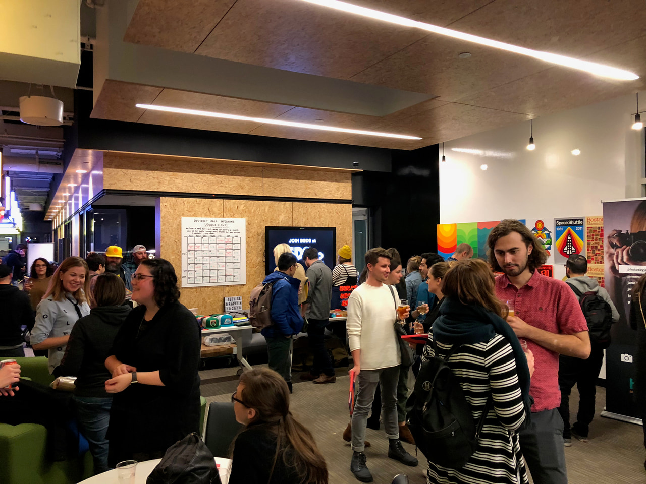 People converse beside a table in a crowded indoor gathering.