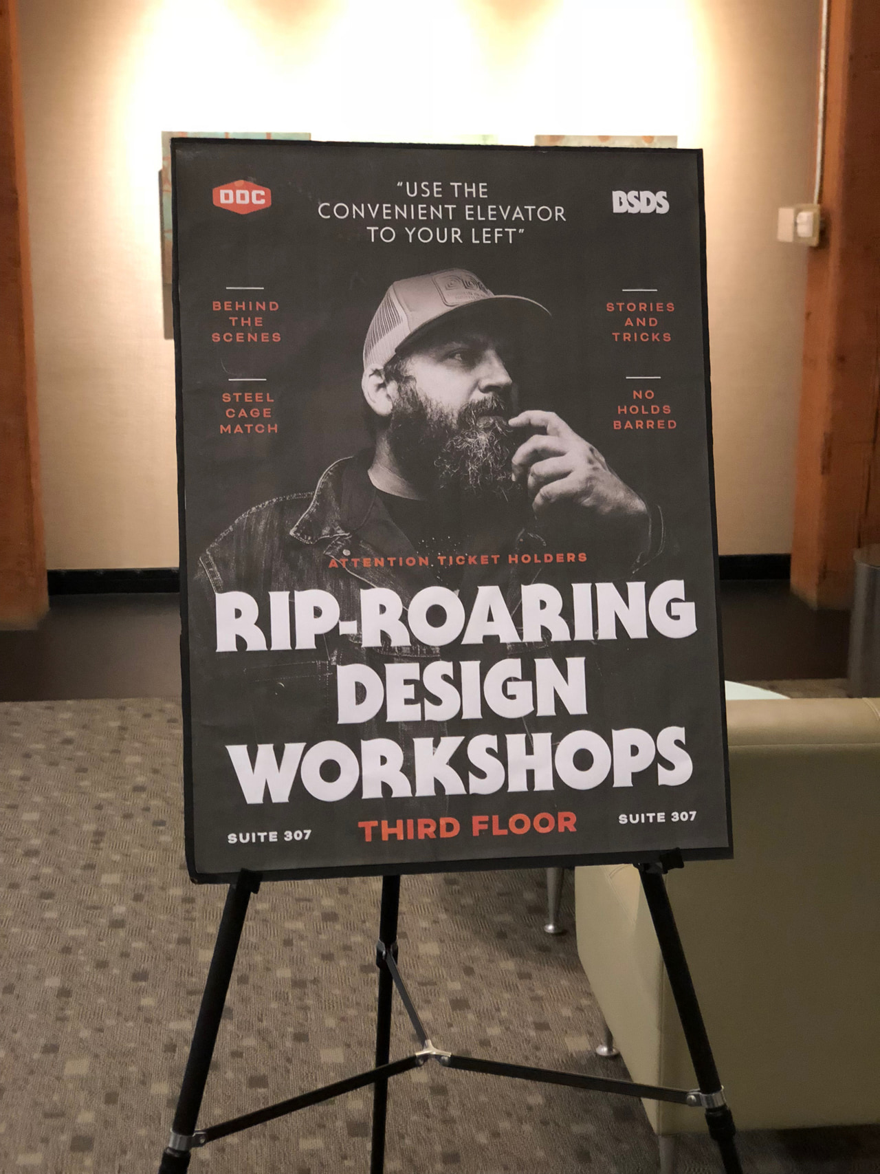 Design workshop poster on an easel, with a portrait above bold white stacked lettering.