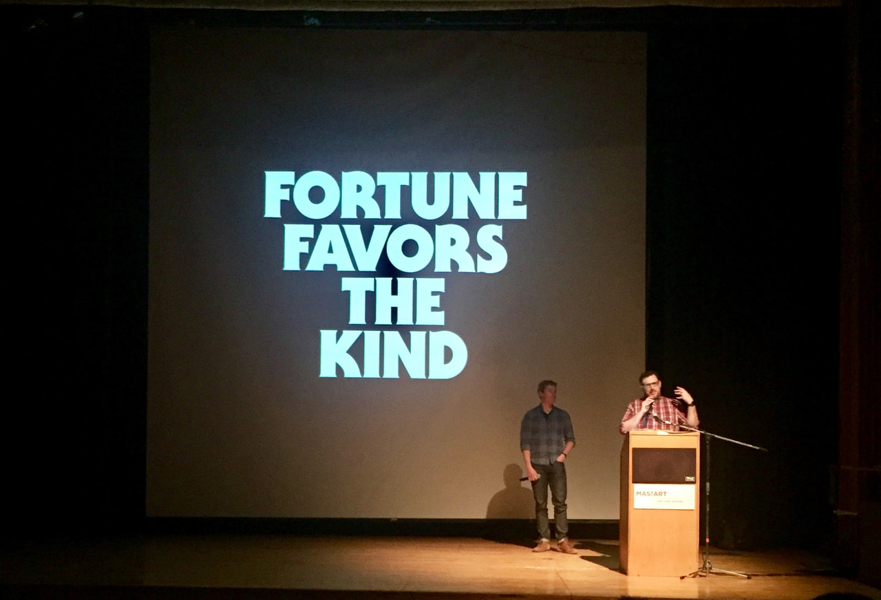 Two speakers onstage beneath projected Fortune Favors the Kind lettering.