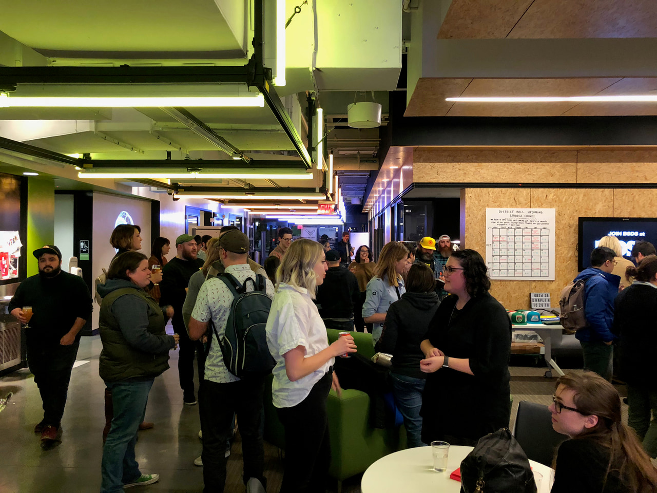 People chat under exposed ceiling beams and green lighting.
