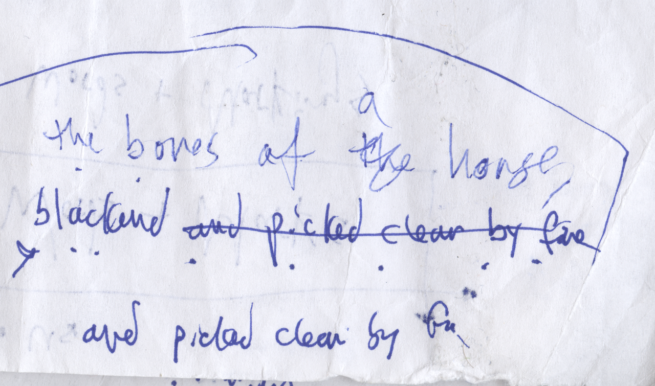 Circled blue handwritten poem draft with a revised article and crossed-out line: The bones of a horse, blackened and picked clean by fire.