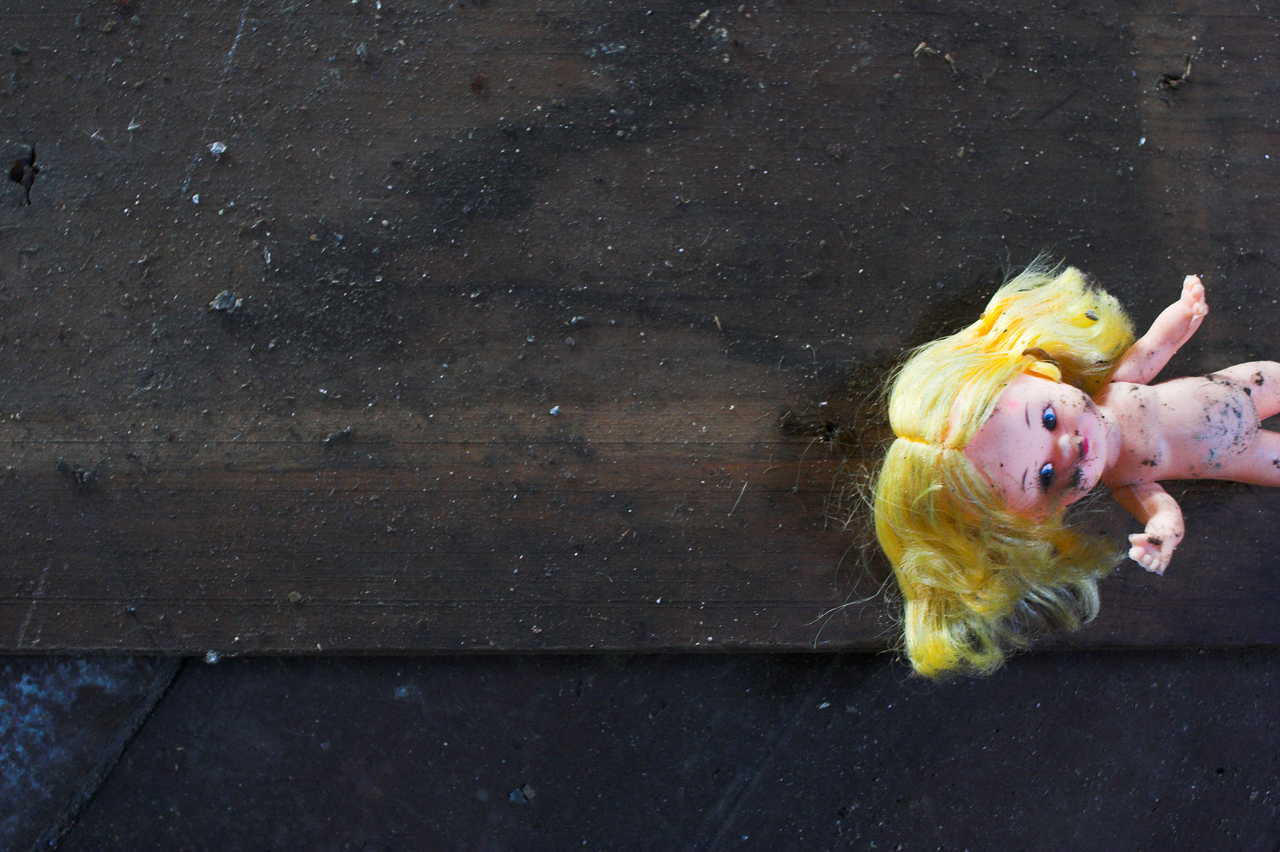 Small yellow-haired doll lying on its side on a dark wooden surface.