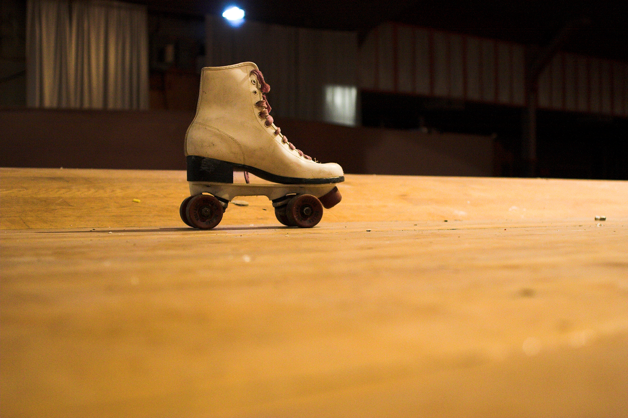 Single cream roller skate with dark wheels on a wooden rink floor.