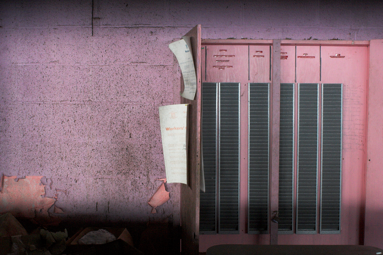 Pink metal lockers against a worn pink wall with peeling paint and debris along the floor.