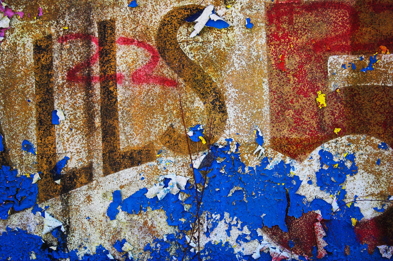 Close-up of peeling bright blue paint and faded red lettering on a rough wall.
