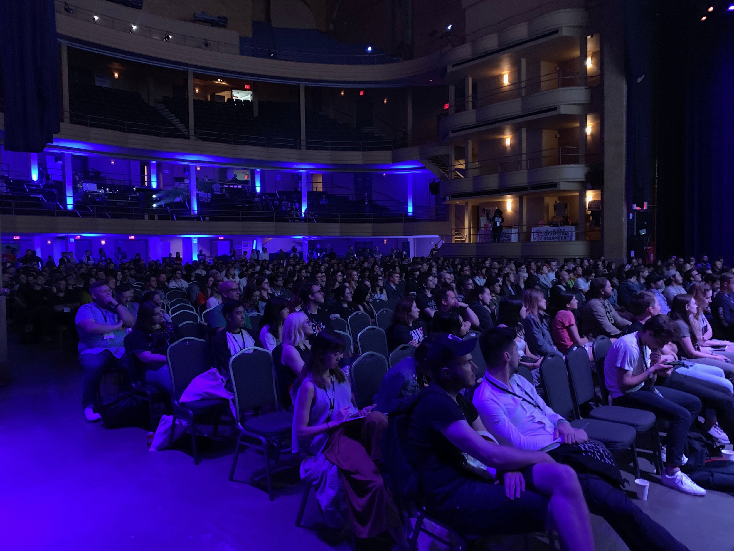 An auditorium audience under blue and purple stage lighting.